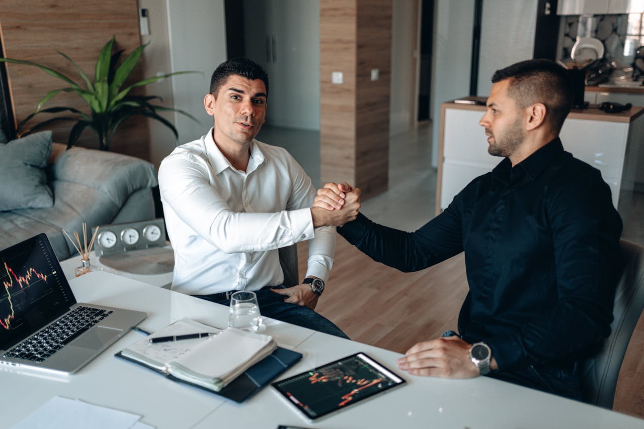Mastering the First Impression: Your intriguing post title goes here Two businessmen shake hands during a meeting in a modern office setting with digital equipment.